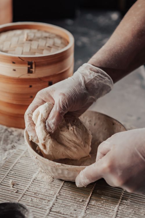 Free Close-up of hands kneading dough in a rustic kitchen setting with bamboo steamer visible. Stock Photo