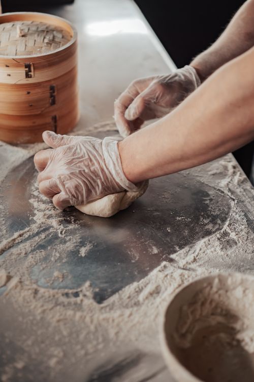 Free Close-up of hands wearing gloves kneading dough on a floured surface. Stock Photo