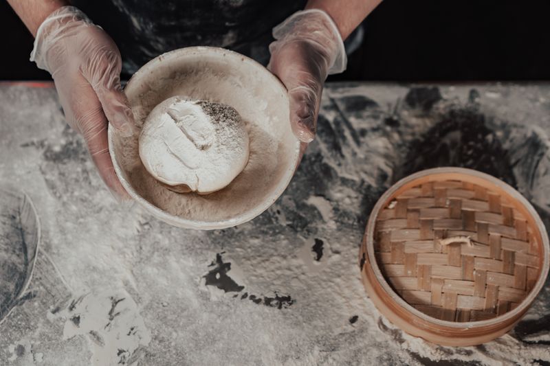 Close-up view of artisan bread dough preparation using bamboo steamer, hands in gloves handling flour.