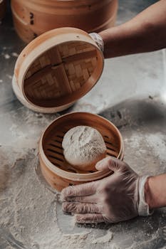 Hands placing dough into a bamboo steamer, ready for cooking preparation.