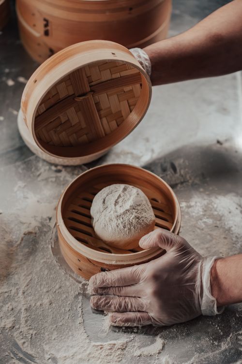 Free Hands placing dough into a bamboo steamer, ready for cooking preparation. Stock Photo
