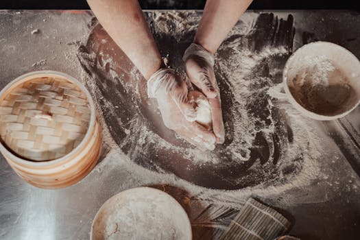 Top view of a chef preparing dough with gloves in a flour-covered kitchen setting.