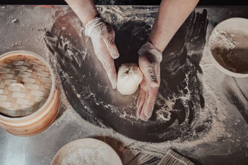 Free Top view of hands making dumplings on a floured surface with bamboo steamer nearby. Stock Photo