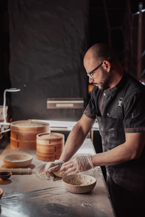 Free A chef skillfully kneads dough in a dimly lit kitchen, showcasing traditional food preparation techniques. Stock Photo