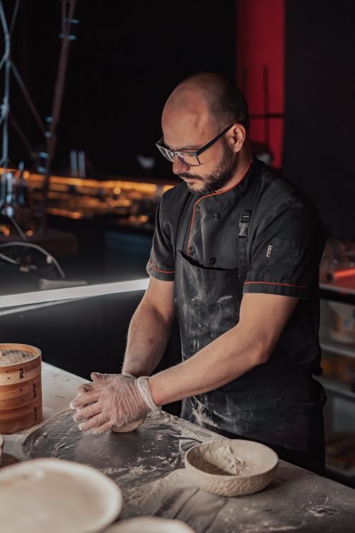 Free Focused chef preparing dough in restaurant kitchen with flour and utensils around. Stock Photo