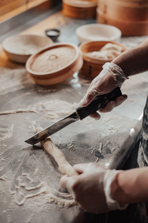 Free Chef cutting dough to make dumplings in a kitchen with bamboo steamers. Stock Photo