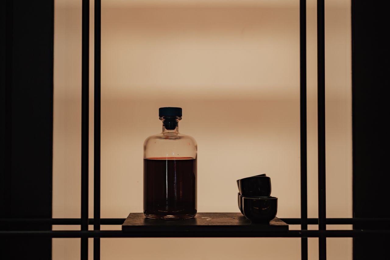 Moody shelf still life with a bottle and stacked cups by Mikhail Nilov on Pexels