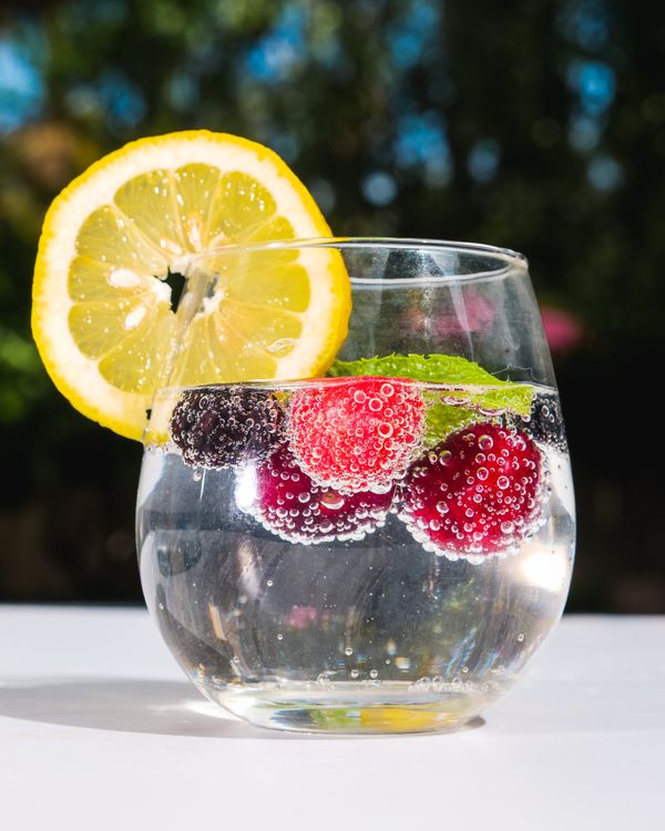 A glass of sparkling water with berries, mint and a slice of lemon