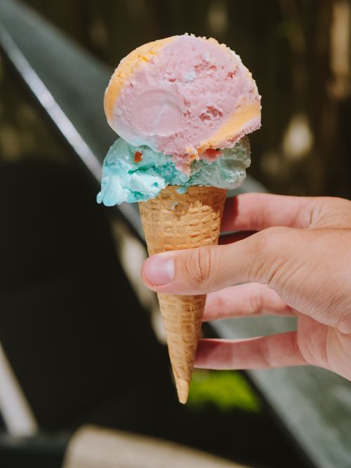 Free Close-up of a colorful ice cream cone held outdoors with blurred background. Stock Photo