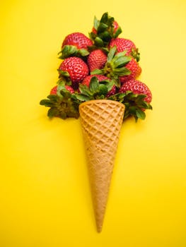 Studio shot of strawberries arranged in an ice cream cone shape against a vivid yellow background.