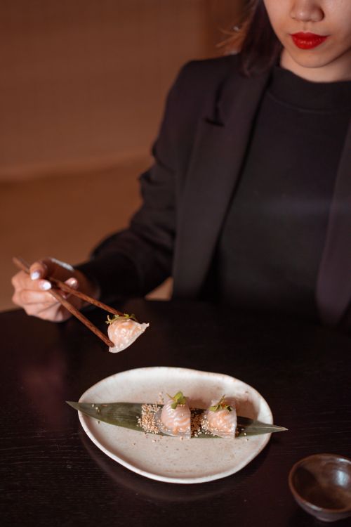 Free A person dining in a restaurant, enjoying Asian dumplings with chopsticks on a beautifully presented plate. Stock Photo
