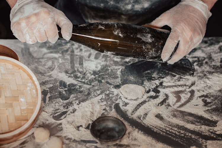 Hands Wearing Latex Gloves Holding A Bottle Near Metal Surface With Flour