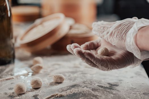 Close-up of hands in gloves molding dough balls on a floured surface with wooden utensils in the background.
