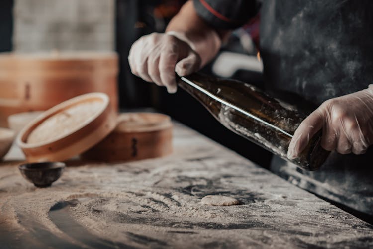 Hands Wearing Latex Gloves Holding A Bottle Near Metal Surface With Flour