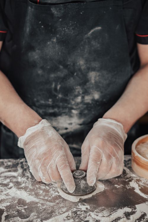 Free A chef wearing gloves works with dough in an indoor kitchen, hands visible. Stock Photo