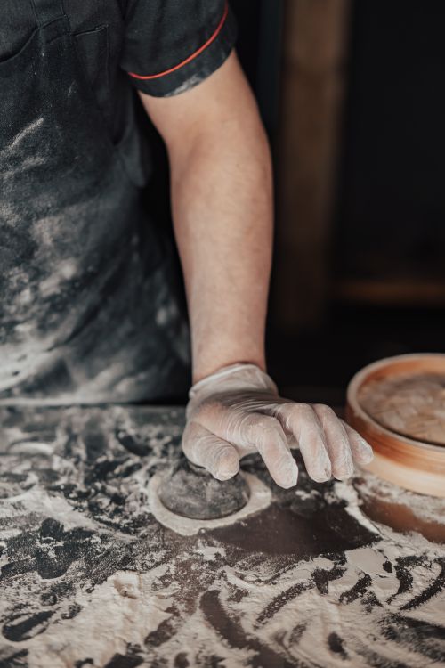 Free A close-up of a gloved hand shaping dough on a flour-covered surface. Stock Photo