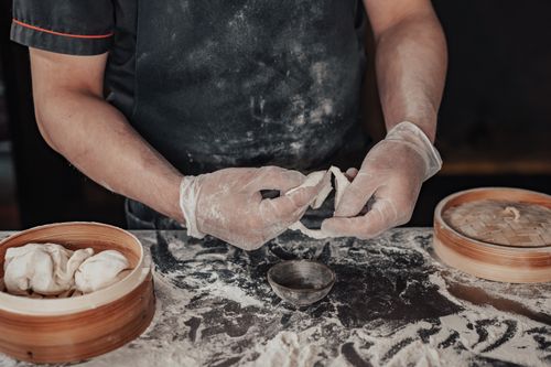 Free A chef wearing gloves expertly shapes dumplings made from dough using a bamboo steamer. Stock Photo