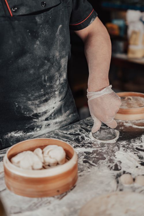 Free A cook wears gloves while preparing dumplings with flour on a kitchen counter. Stock Photo