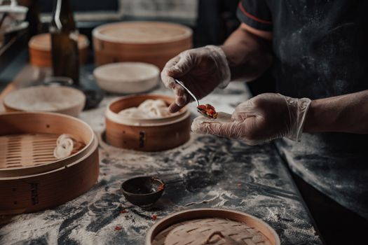 Chef uses gloves to fill dumplings in a kitchen with bamboo steamers and flour dust.