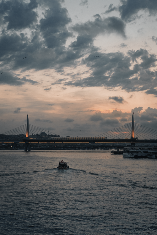 Free Picturesque landscape of bridge over river with vessel floating on water and cityscape far away in cloudy evening Stock Photo