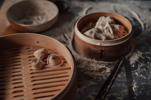 Handmade dumplings resting in a bamboo steamer surrounded by flour in a cozy indoor setting.
