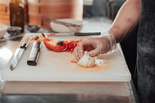 A Person Holding Garlic on White Chopping Board