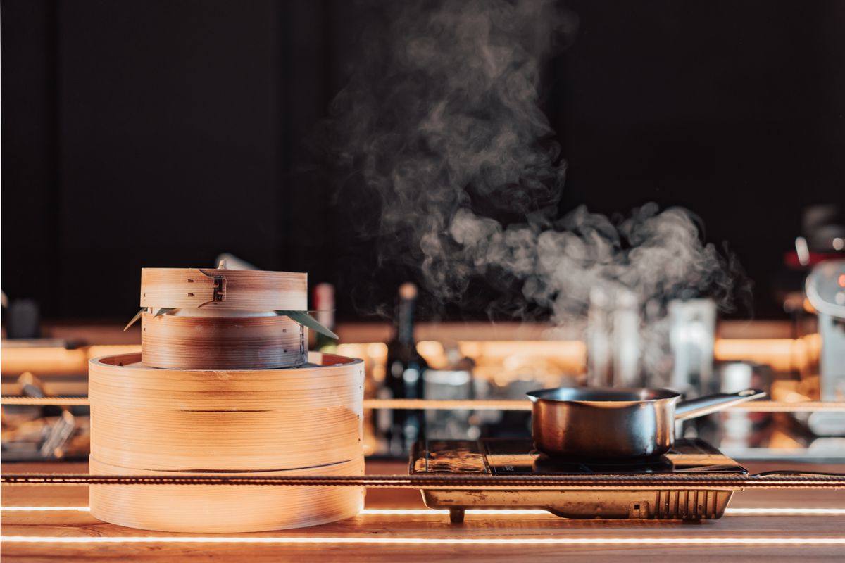 Bamboo steamer releasing steam in a dark kitchen — photo by Mikhail Nilov on Pexels