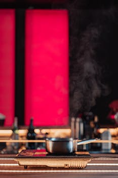 A contemporary kitchen scene featuring a steaming pot on an electric stove under vibrant red lighting.