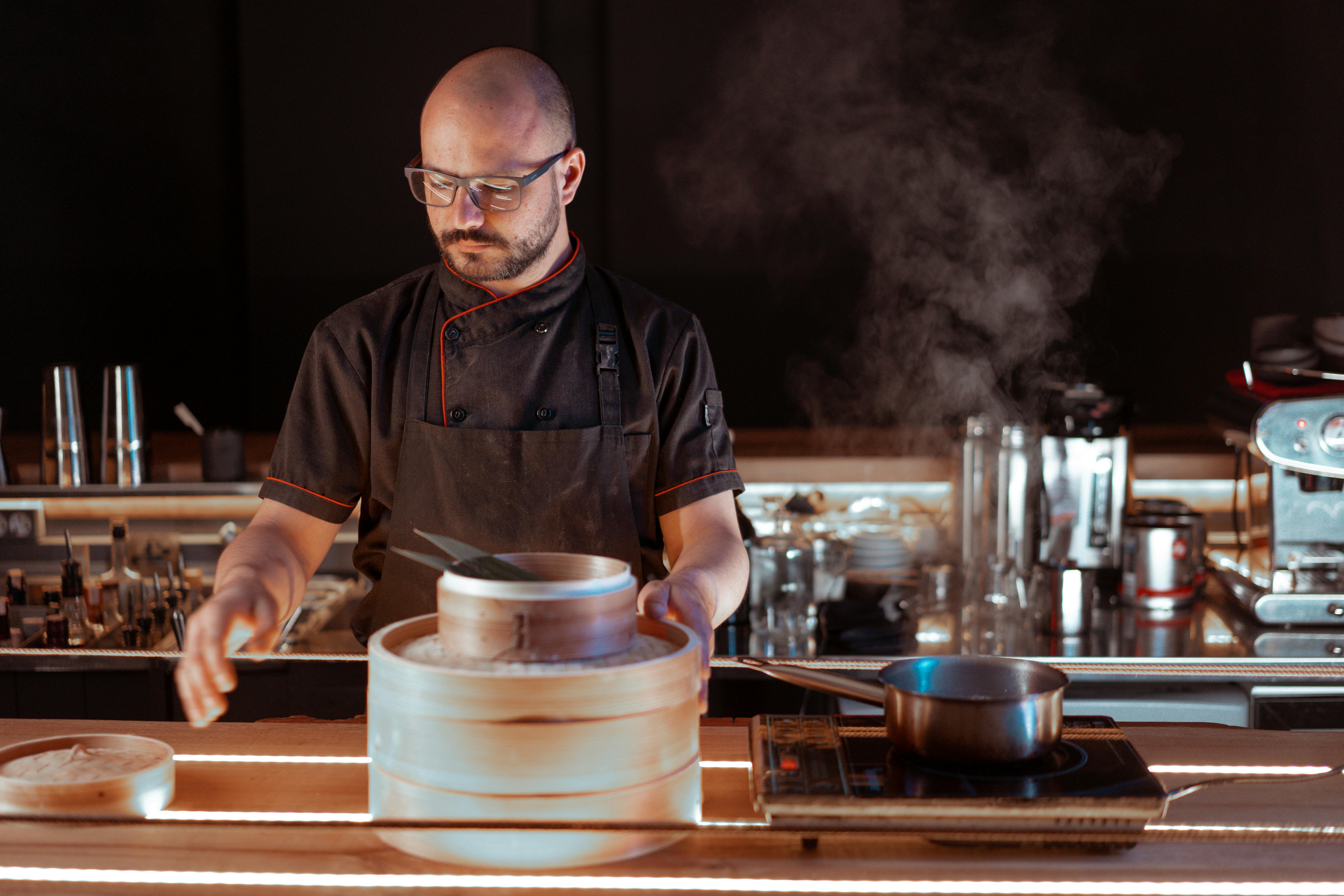 A skilled chef in a modern kitchen making dim sum with steam rising.
