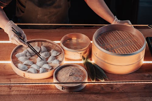 Person Preparing Dumplings Using Chopsticks on Bamboo Steamer