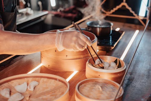 Person Preparing Dumplings Using Chopsticks on Bamboo Steamer