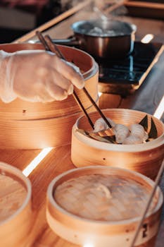 Close-up of a chef using chopsticks to prepare fresh dumplings in a bamboo steamer indoors.