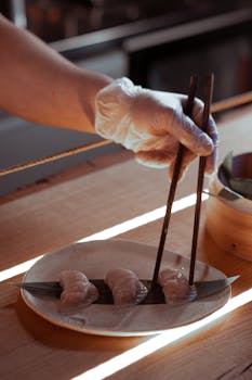 Close-up of a gloved chef serving dim sum on plate using chopsticks in a restaurant.