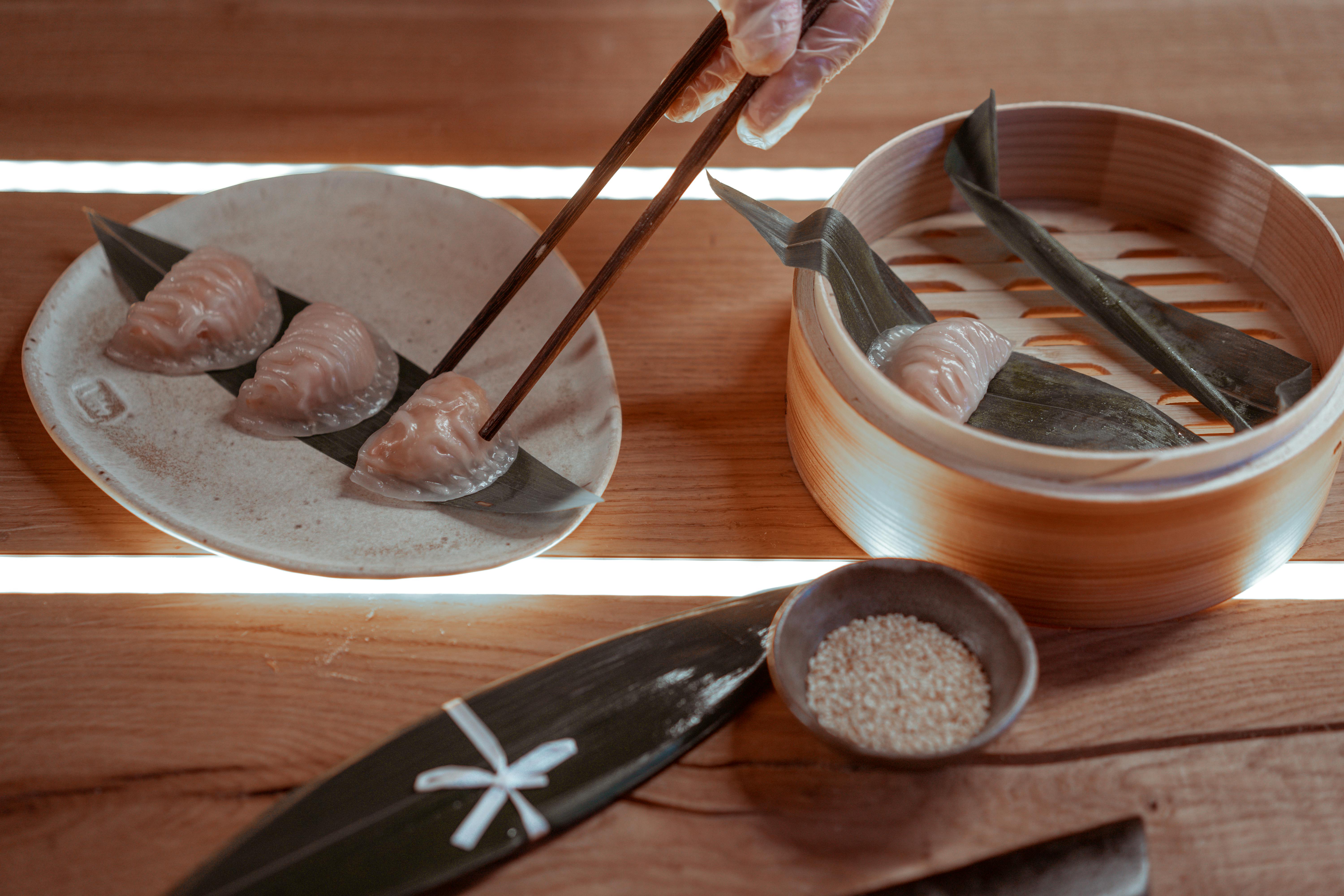 Close-up of bamboo steamer with dumplings, chopsticks, and sesame seeds.