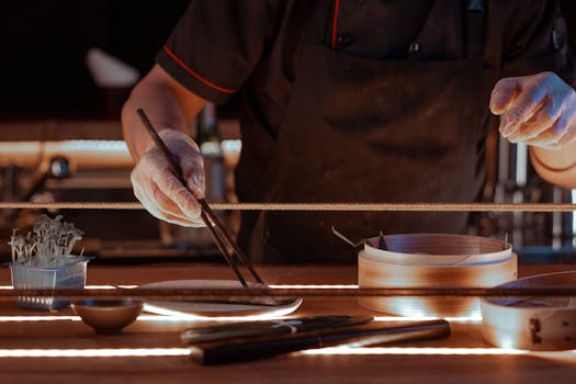Chef using chopsticks to prepare Asian cuisine in a dimly lit kitchen setting.