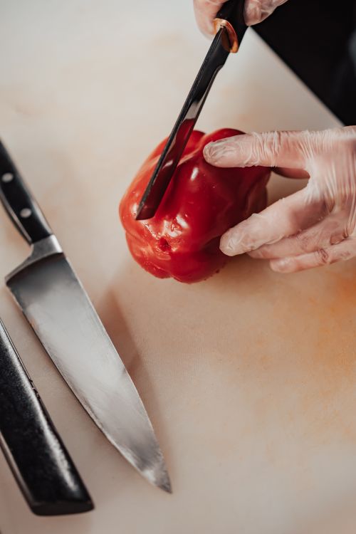 Free Close-up of a chef slicing a red bell pepper with knives on a cutting board in a commercial kitchen. Stock Photo