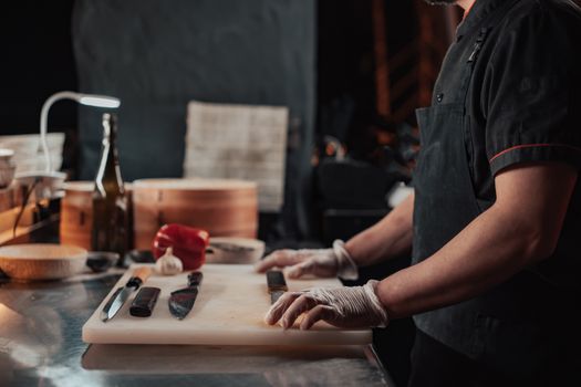 A chef in gloves preparing ingredients on a cutting board in a dimly lit kitchen.
