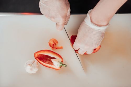 Free Close-up of hands with gloves slicing red pepper and garlic on a cutting board. Stock Photo