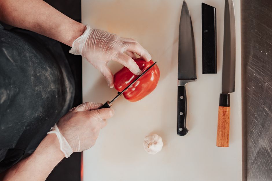 Top view of a chef slicing red pepper on a cutting board with knives, showcasing culinary skills.