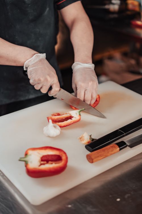 Free A chef wearing gloves slicing red bell pepper on a cutting board with a knife. Stock Photo