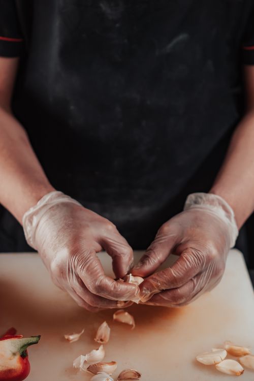 Free A person wearing gloves peels garlic on a cutting board with precision and focus. Stock Photo