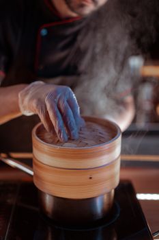 A chef using a bamboo steamer with visible steam, highlighting culinary expertise.