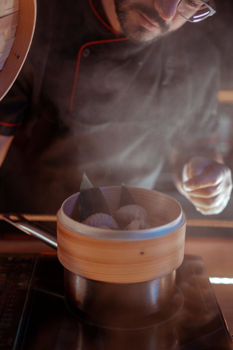 Man Looking At Cooked Dumplings In A Bamboo Steamer