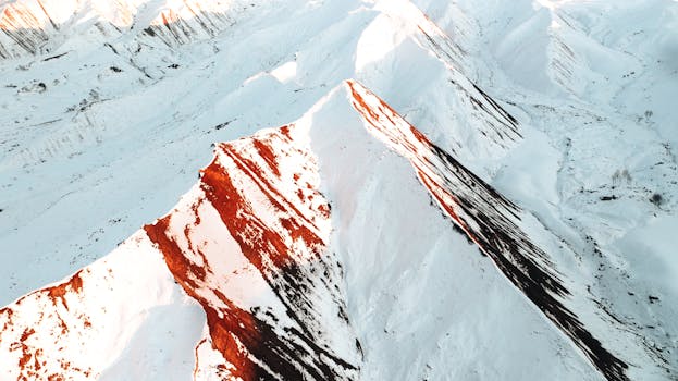 Stunning aerial view of snow-covered mountains with red rock peaks in Türkiye's winter landscape.
