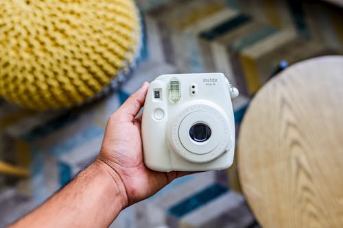 Close-Up Photo of a Person's Hand Holding a White Instant Camera