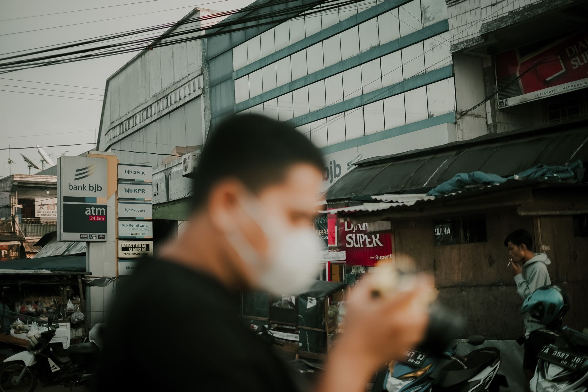 Side view of blurred unrecognizable male in medical mask with photo camera standing on street in local district during pandemic