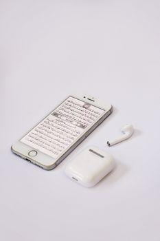 Minimalist shot of a smartphone with text and wireless earbuds on a white surface, conveying simplicity.
