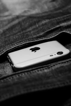 Close-up of a smartphone partially visible in denim pocket, grayscale effect.