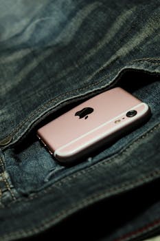 A rose gold smartphone peeking out from a denim blue jeans pocket, highlighting modern lifestyle.
