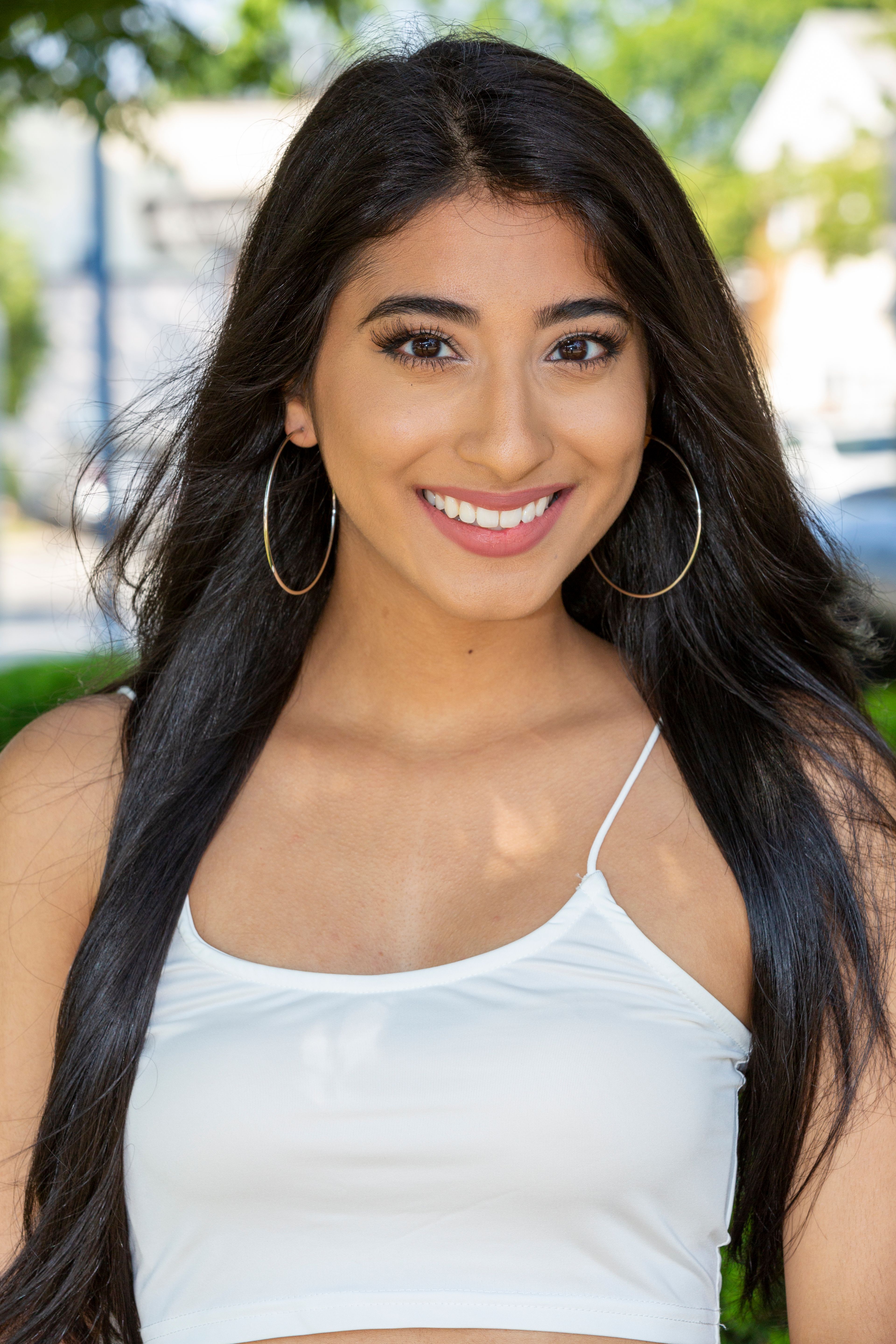 Outdoor portrait of a smiling woman with long hair and hoop earrings, exuding warmth and confidence.